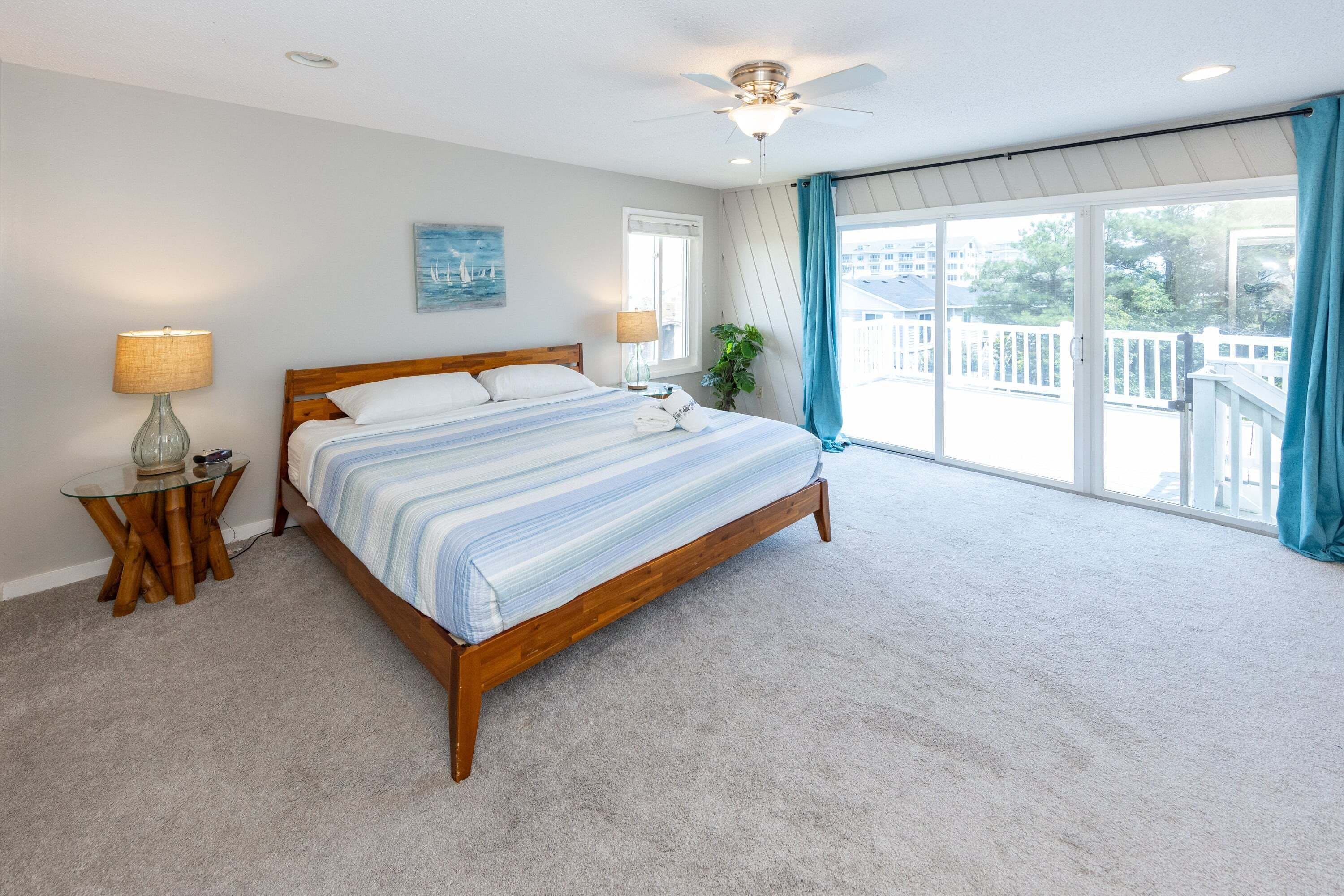 A bedroom with a large bed, two bedside tables, a ceiling fan, and a view of the outside.