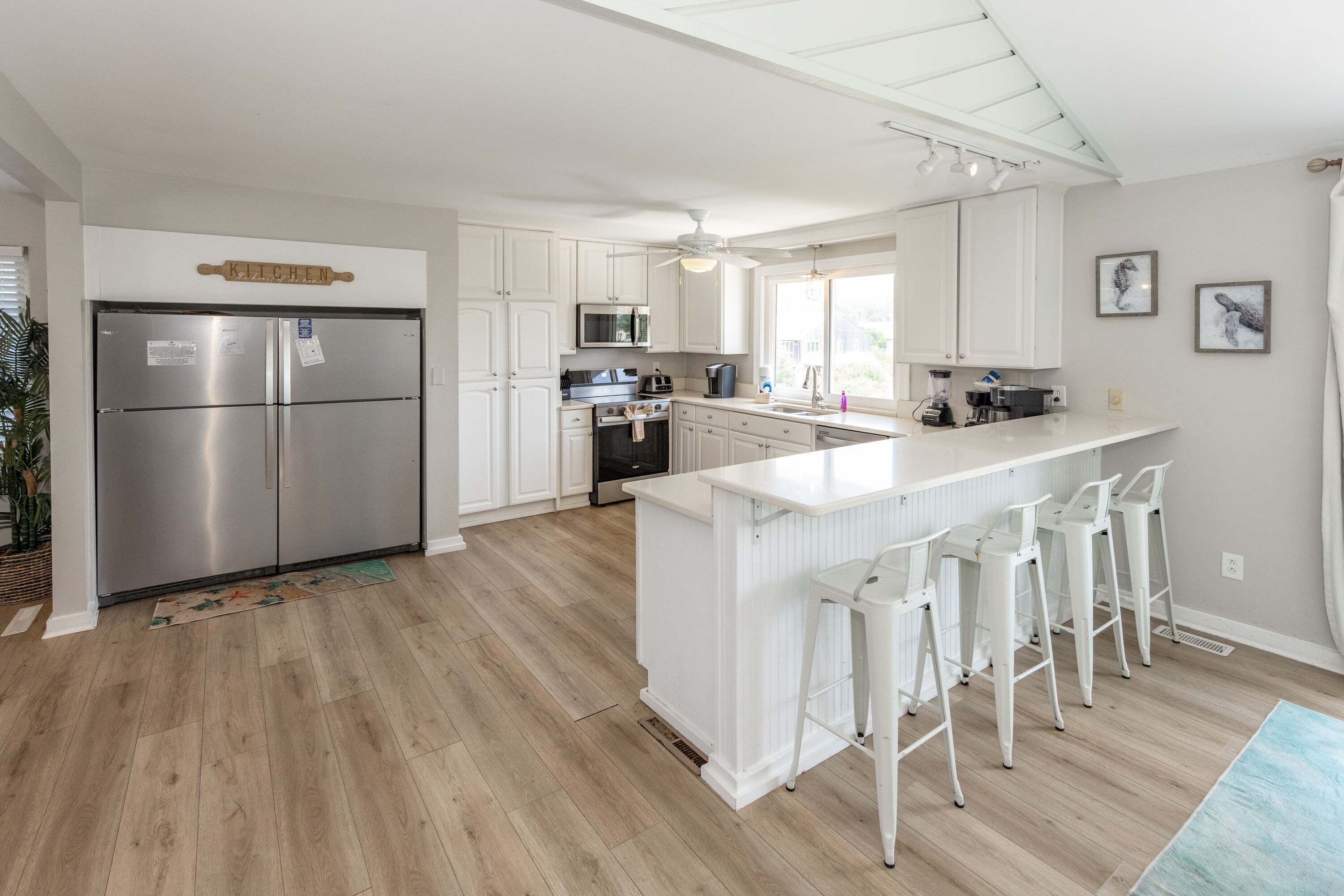 Une cuisine moderne avec des meubles blancs, des appareils en acier inoxydable et un coin bar avec des tabourets.
