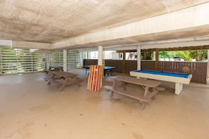 An outdoor covered area with picnic tables and a pool table.
