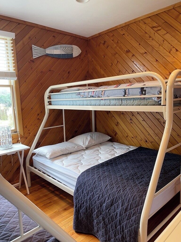 Een slaapkamer met stapelbed, houten wand, een visdecoratie en een klein tafeltje met een glas.
