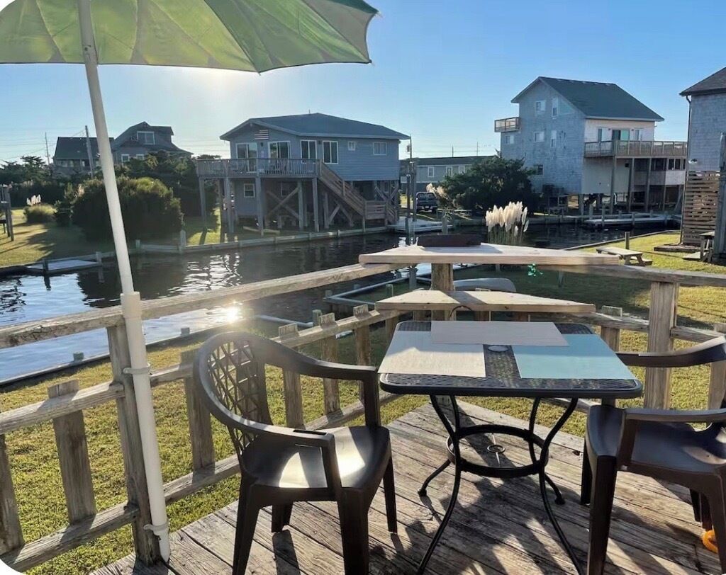 An outdoor deck with a table and chairs, overlooking a water body and residential buildings.