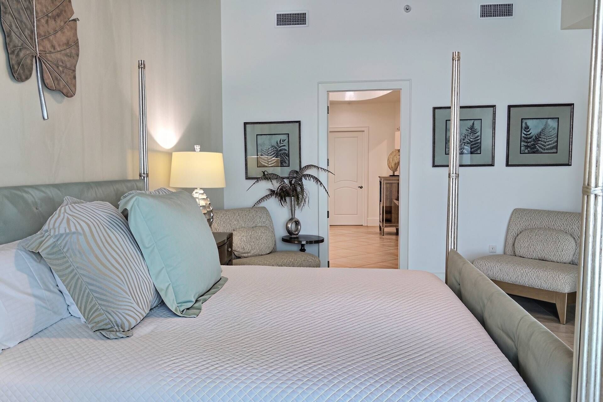Un dormitorio con cama, mesita de noche, lámpara, sillón y cuadros en la pared.