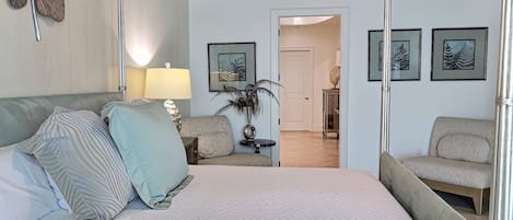 Un dormitorio con cama, mesita de noche, lámpara, sillón y cuadros en la pared.