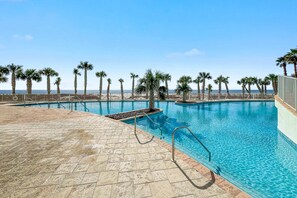 A pool area with clear blue water, palm trees, and a view of the ocean. - Turquoise Place D2201 | Pools, Lazy River + Balcony Hot Tub & Grill (Orange Beach)