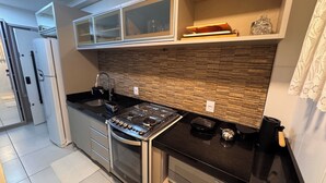 A modern kitchen with a gas stove, a built-in oven, a sink, and a microwave. - Condomínio Henrique I (Balneário piçarras)