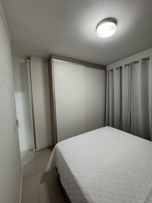 Un dormitorio con cama, armario, puerta y una lámpara en el techo.