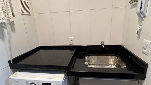 A compact kitchen with a washing machine, a sink, and a telephone. - Condomínio Henrique I (Balneário piçarras)