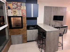 Una cocina compacta con una isla central, taburetes de bar, un televisor integrado y decoraciones de pared de estilo vintage.