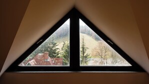 A triangular window with a view of a building and trees. - Sia Mountain Apartment (Predeal)