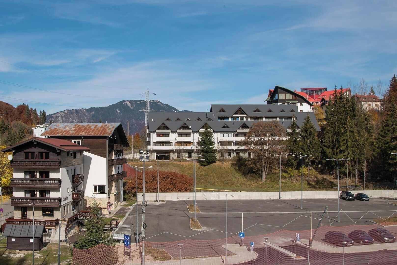 A multi-story building with balconies, a parking lot, and a mountain in the background.