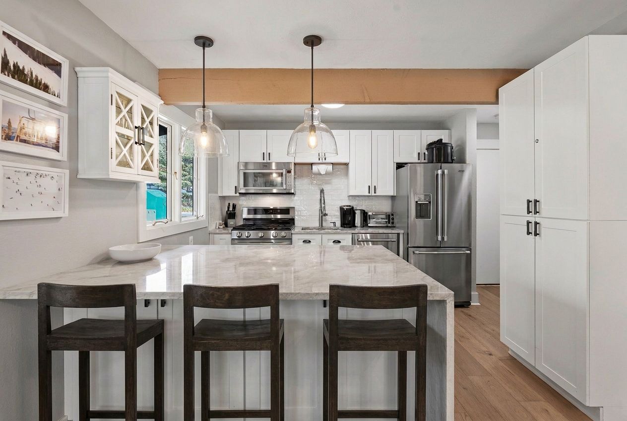 A modern kitchen with a central island, white cabinetry, stainless steel appliances, and pendant lighting.