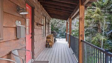 Une véranda en bois avec une porte rouge, une pile de bois de chauffage et un barbecue.