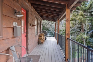 Une véranda en bois avec une porte rouge, une pile de bois de chauffage et un barbecue.