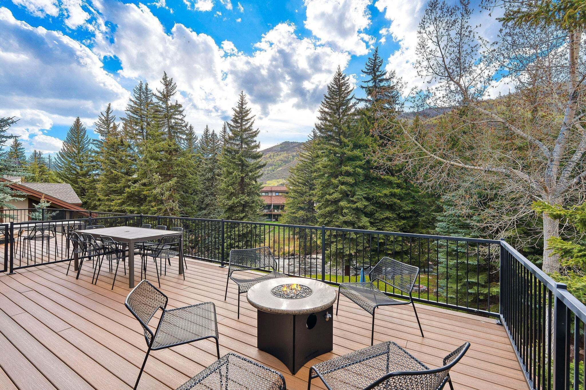 Une terrasse dotée de mobilier d’extérieur et d’un foyer, entourée d’arbres et offrant une vue sur la montagne.