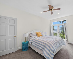 A bedroom with a bed, a ceiling fan, a window with curtains, and a door.