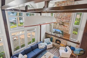 A cozy living room with a fireplace, a blue sofa, and a view of the outdoors through large windows.