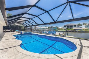 A swimming pool with a covered area, lounge chairs, and a view of a residential area. - Modern Waterfront Retreat with Pool, Spa & Canal Access - FMB - Sea-O-Siesta - Roelens (Fort Myers Beach)