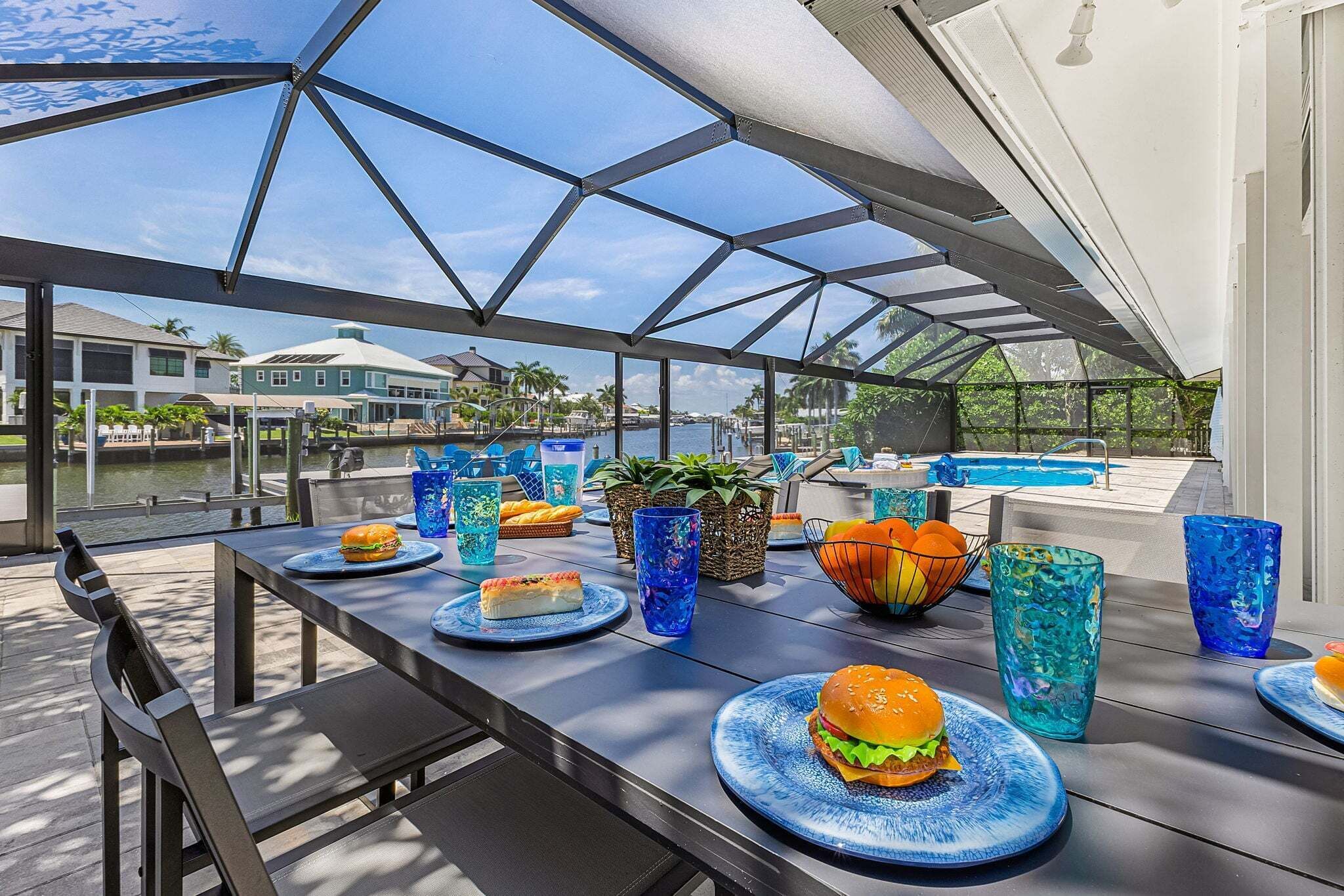An outdoor dining area with a glass roof, tables with plates of food, and a pool in the background.