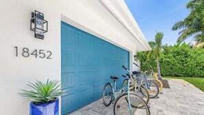 Un garage d’habitation avec une porte bleue, une plante en pot et des vélos garés à l’extérieur.