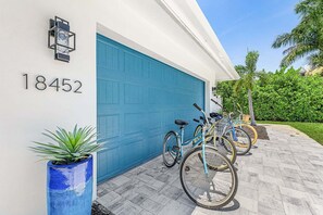 A residential garage with a blue door, a potted plant, and bicycles parked outside. - Modern Waterfront Retreat with Pool, Spa & Canal Access - FMB - Sea-O-Siesta - Roelens (Fort Myers Beach)