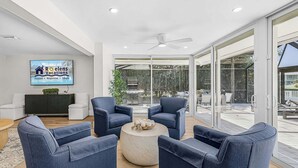 Un salon moderne doté d’une grande porte vitrée donnant sur un espace extérieur, d’un téléviseur à écran plat fixé au mur et d’un ventilateur de plafond.