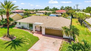 A residential house with a tiled roof, a garage, and a front yard with a palm tree. - Gulf Access Escape with Heated Pool, Dock & Kayaks - Villa Maria - Roelens (Cape Coral)