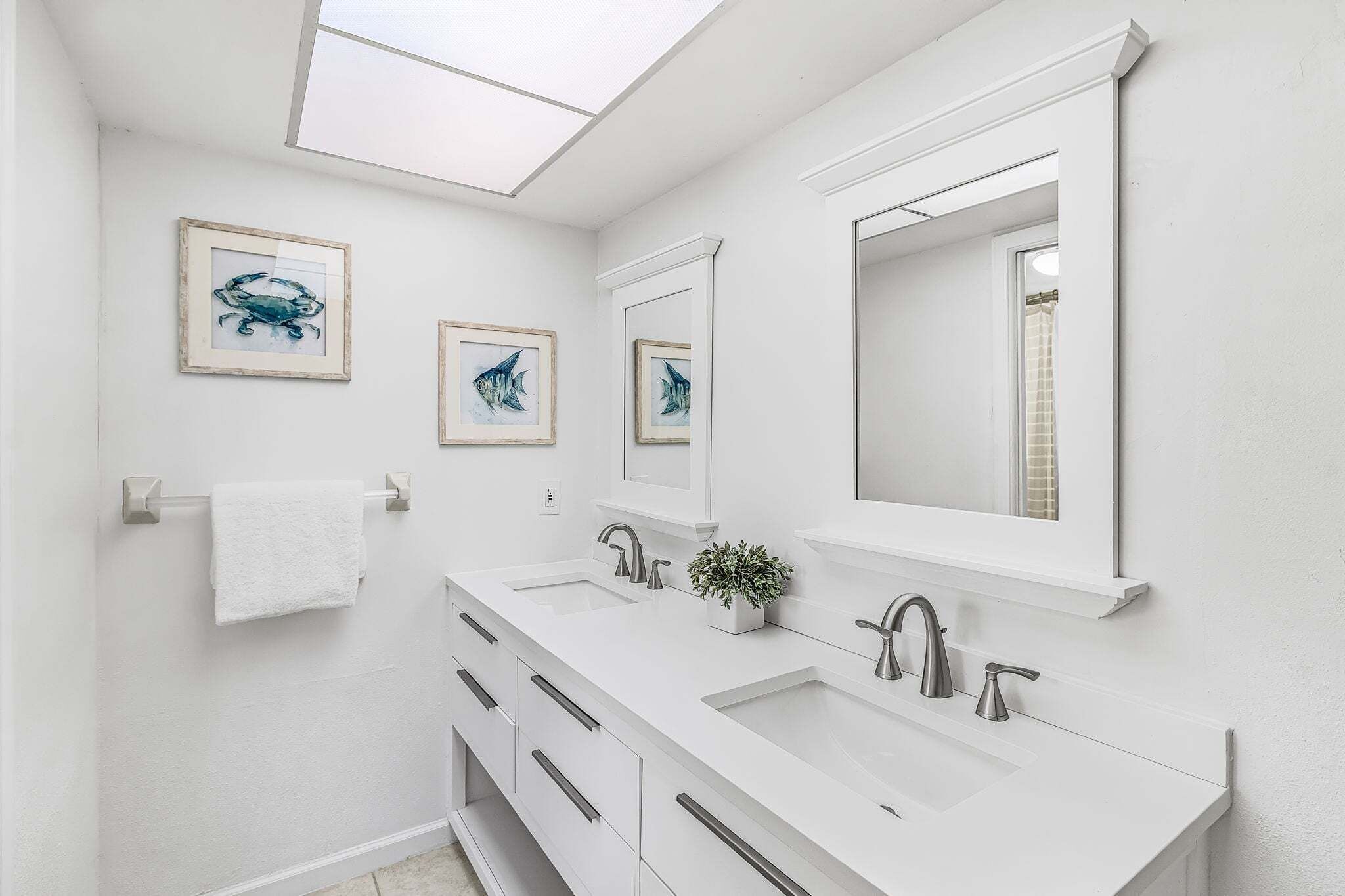 A modern bathroom with two sinks, a large mirror, and framed artwork on the wall.
