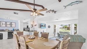 A spacious dining area with a wooden table and chairs, a ceiling fan, and a kitchen in the background. - Gulf Access Escape with Heated Pool, Dock & Kayaks - Villa Maria - Roelens (Cape Coral)