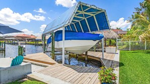 A boat docked at a wooden pier with a covered area, surrounded by water and greenery. - Gulf Access Escape with Heated Pool, Dock & Kayaks - Villa Maria - Roelens (Cape Coral)