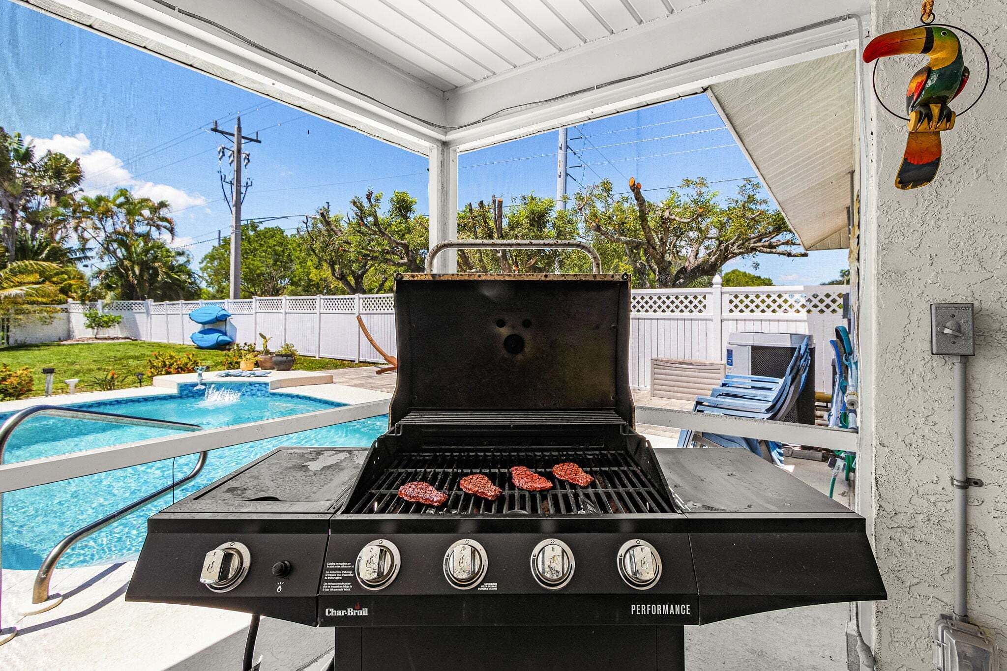 Una parrilla al aire libre con cuatro quemadores, una piscina y un patio cubierto.