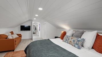 A modern bedroom with a large bed, a sofa, and a television on the wall.