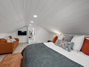 A modern bedroom with a large bed, a sofa, and a television on the wall.