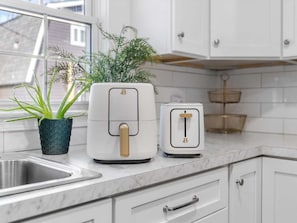 A kitchen with white cabinets, a marble countertop, a sink, a plant, and two appliances.