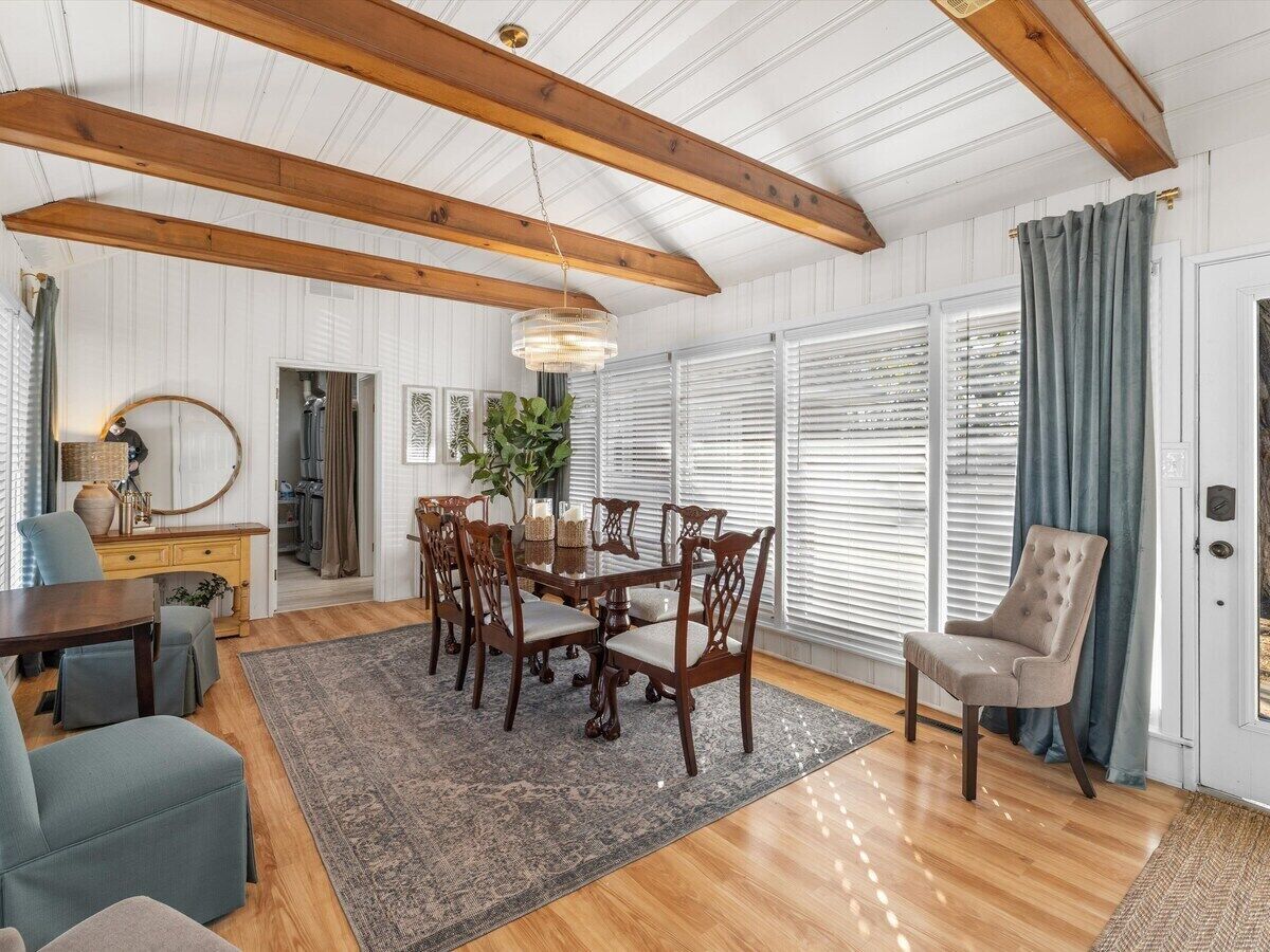 A dining area with a wooden table and chairs, a chandelier, and a view through large windows.