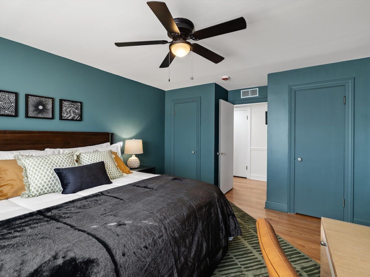 A bedroom with a bed, a ceiling fan, a nightstand, a lamp, and a door.