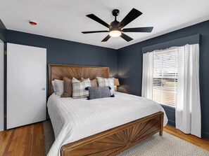 A bedroom with a bed, a ceiling fan, a window with blinds, and a door.