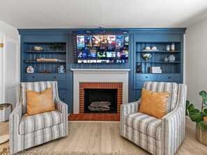 A living room with a fireplace, two striped armchairs, a blue entertainment wall, and a wooden floor.