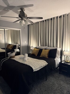 A hotel room with a bed, a nightstand, a lamp, a ceiling fan, and curtains.