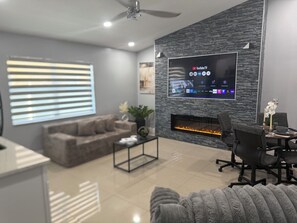 Un salon moderne doté d’un téléviseur à écran plat fixé sur un mur texturé, d’une cheminée, d’un canapé et d’un coin repas avec une table et des chaises.