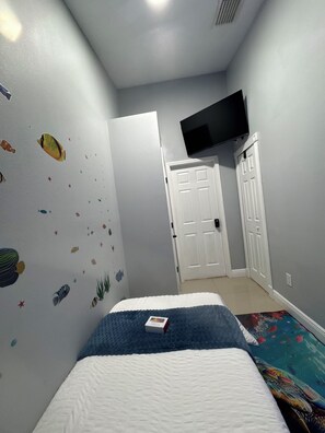 Une chambre à coucher avec un lit, un téléviseur fixé au mur et une porte donnant sur une autre pièce.