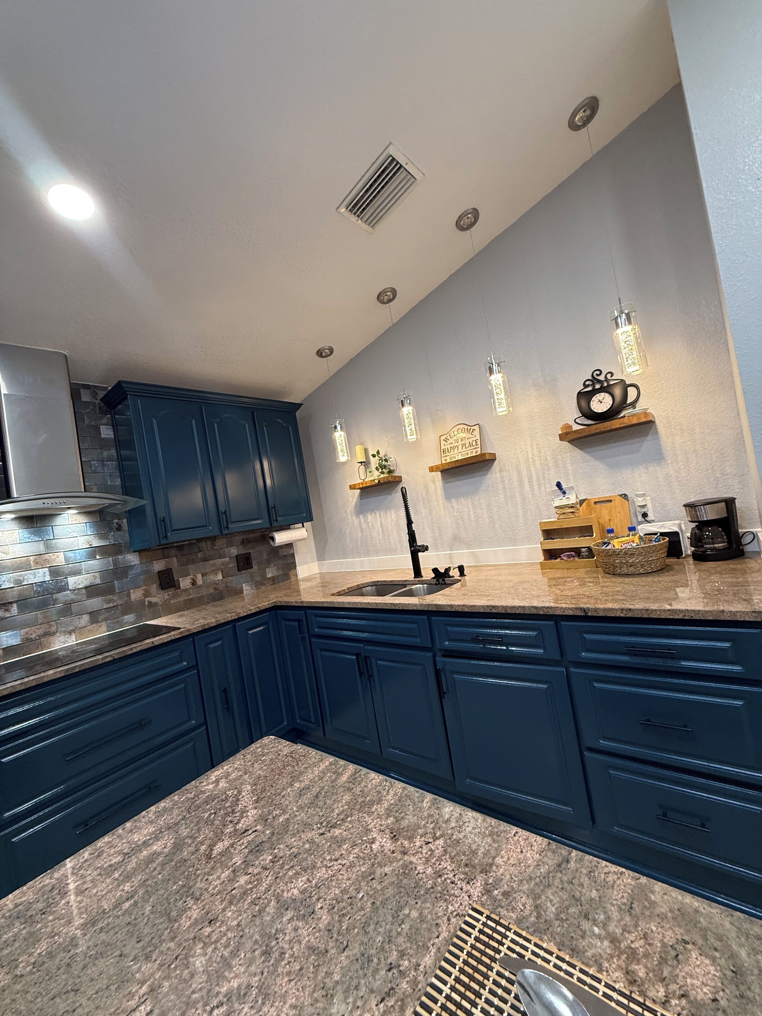 Une cuisine moderne avec des meubles de couleur bleu foncé, un plan de travail en granit et des luminaires suspendus.