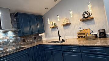 Une cuisine moderne avec des meubles de couleur bleu foncé, un plan de travail en granit et des luminaires suspendus.
