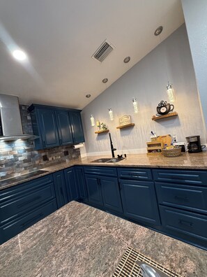 Une cuisine moderne avec des meubles de couleur bleu foncé, un plan de travail en granit et des luminaires suspendus.