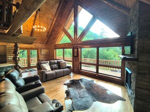 Ein Holzblockhaus-Interieur mit einem großen Sofa, einem Ledermatte und einem Kamin aus Stein.