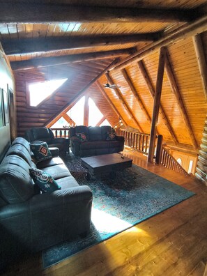 Ein Loft-Zimmer mit schrägem Dach, Holzbalken, einer Sofagarnitur und einer Treppe zu einer erhöhten Ebene.