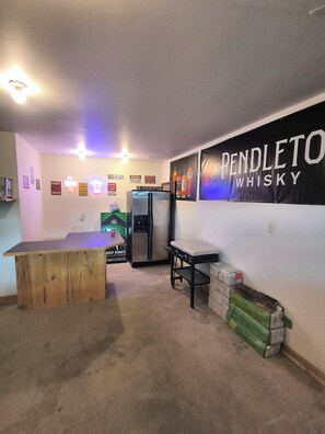 Una habitación con una barra de madera, un refrigerador y una pared con un cartel grande.