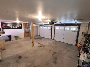 A garage with three white doors, a wooden bench, a wall-mounted sign for Pendleton Whiskey, and a ceiling light fixture. - Beautiful Log House 3+ bedroom house in Deadwood with 2 stall garage (Deadwood)