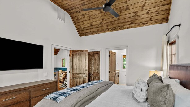 Ein Schlafzimmer mit Holzboden, einem Bett mit vielen Kissen, einem Schminktisch und einem an der Wand befestigten Fernseher.