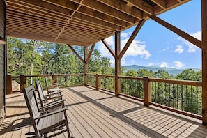 A wooden deck with a railing overlooking a forested area and distant mountains. - Ridge & Repeat Lodge at Eagles Nest - hot tub, in+out fireplace, firepit, views (Banner Elk)