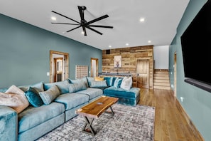 A modern living room with a sectional sofa, a wooden coffee table, and a ceiling fan. - Ridge & Repeat Lodge at Eagles Nest - hot tub, in+out fireplace, firepit, views (Banner Elk)